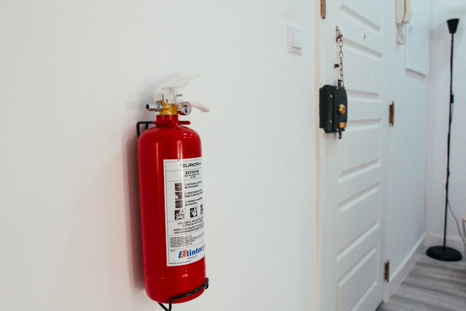 Smoke detector beeping fire-safety context: a red fire extinguisher mounted on a clean white wall in a modern apartment hallway