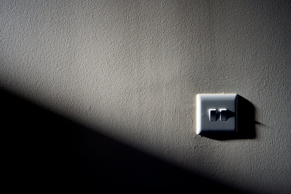 Light switch not working detail: close-up of a single light switch on a textured wall under contrasting light, illustrating the minimalist hardware that fails in a light switch not working complaint