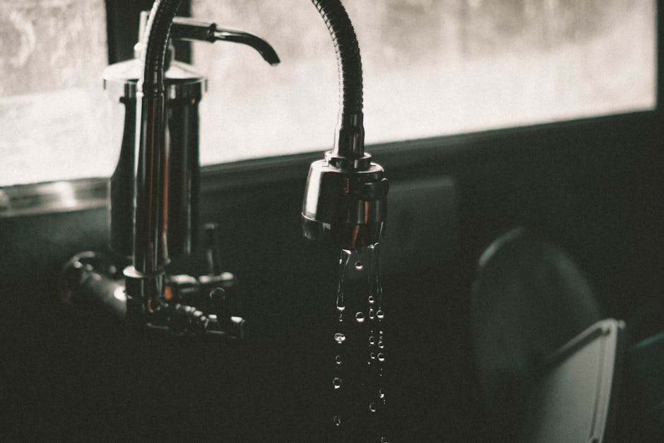 Leaking faucet kitchen scenario: close-up of a kitchen faucet with water droplets falling into a sink, the classic single-lever leaking faucet symptom
