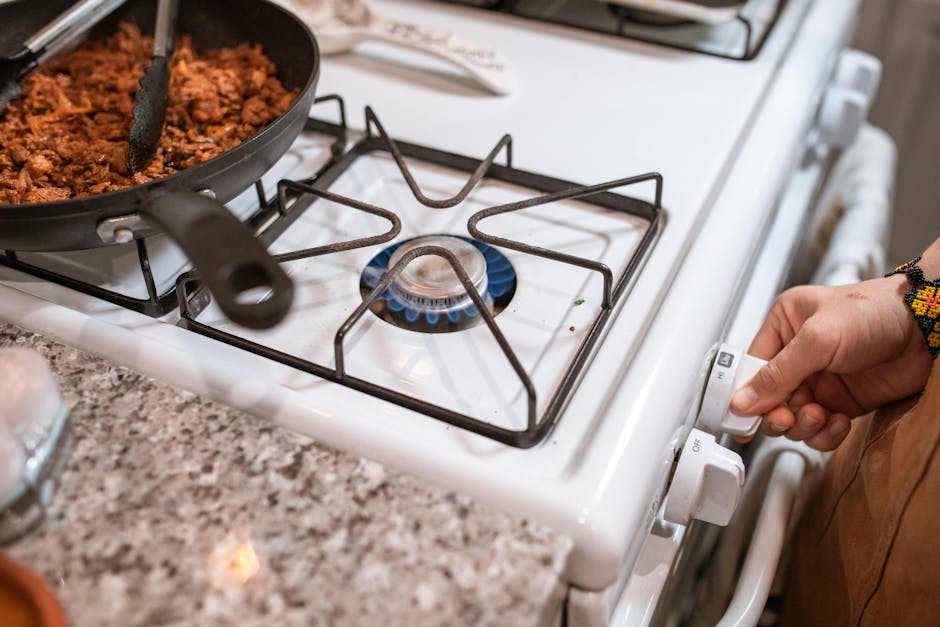Stove burner won't light cooking context: close-up of a hand operating a gas stove with meat cooking in a pan, the everyday use case where a stove burner won't light interrupts