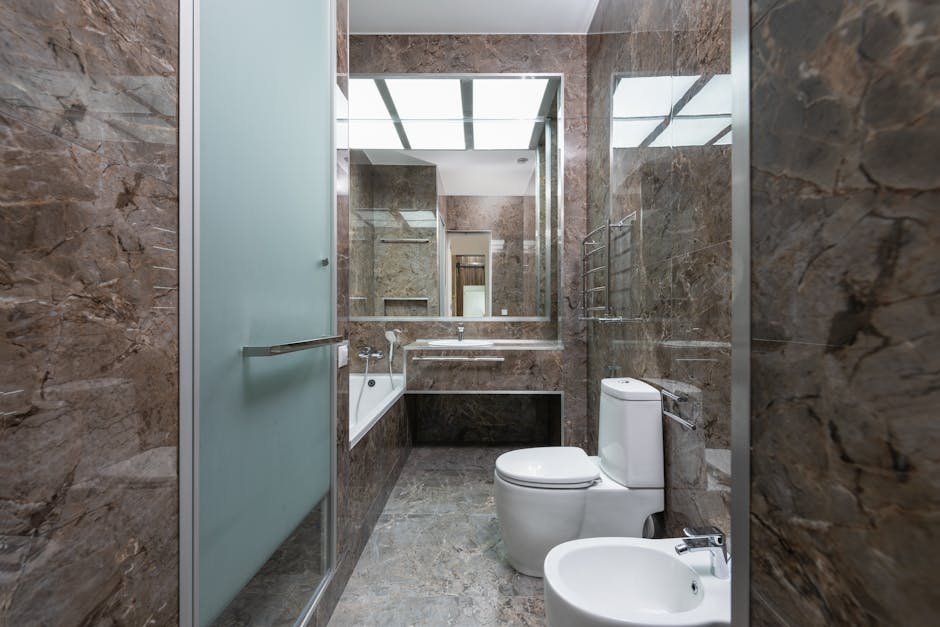 Toilet keeps clogging context: spacious bathroom with marble walls, a glass door, and modern fixtures including a sink and toilet, the typical environment where a toilet keeps clogging on a schedule