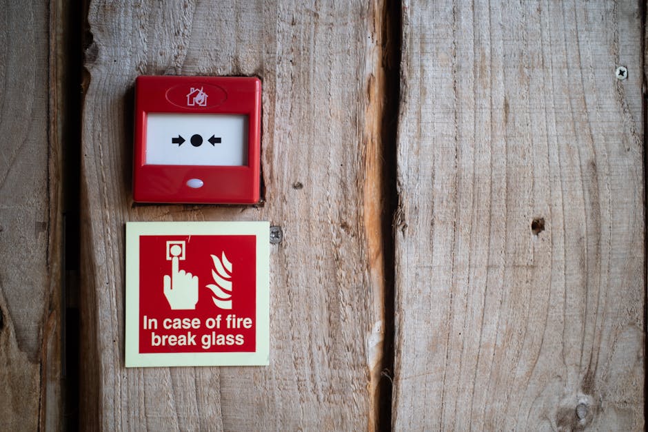 Smoke detector beeping context: a red fire alarm and warning sign mounted on a rustic wooden wall for indoor safety awareness