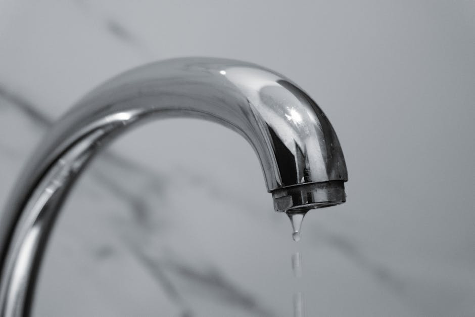 Leaking faucet: close-up shot of a modern chrome bathroom faucet with water dripping steadily from the spout, the classic homeowner symptom