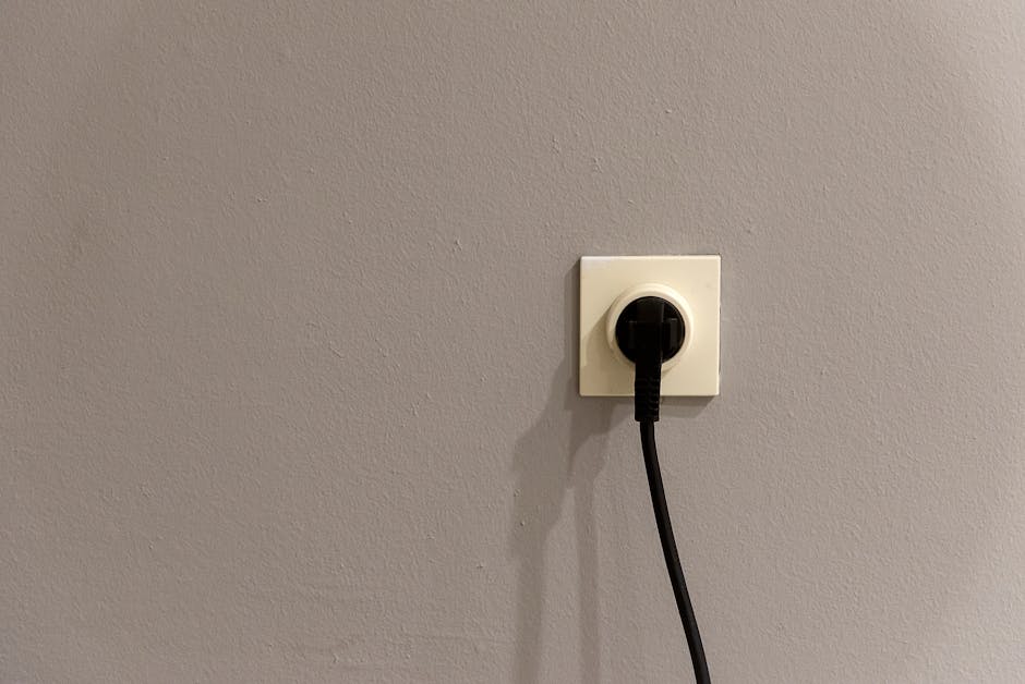Outlet sparking: a standard white residential duplex receptacle on a neutral wall with a plug halfway inserted, the typical setup where an outlet sparking complaint first shows itself as a quick blue flash at the prongs the moment the circuit closes