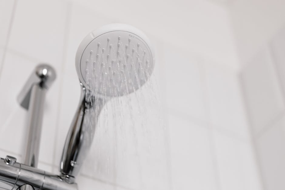 Shower drain smells: stylish clean shower head with water flow in a white tiled bathroom, the typical setting for a shower drain smells diagnosis where everything looks clean but the air does not