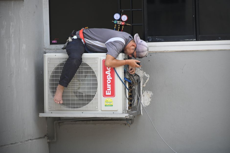 HVAC technician servicing a central air conditioner and explaining AC replacement cost to a homeowner